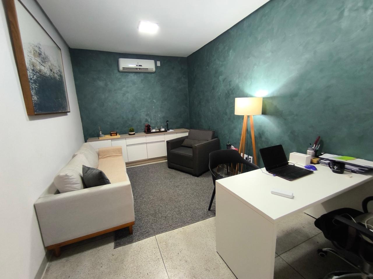 Consultório com parede verde, sofá e mesa de atendimento